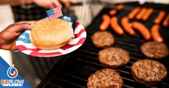 hamburgers and hotdogs being grilled, while a person holds a hamburger bun