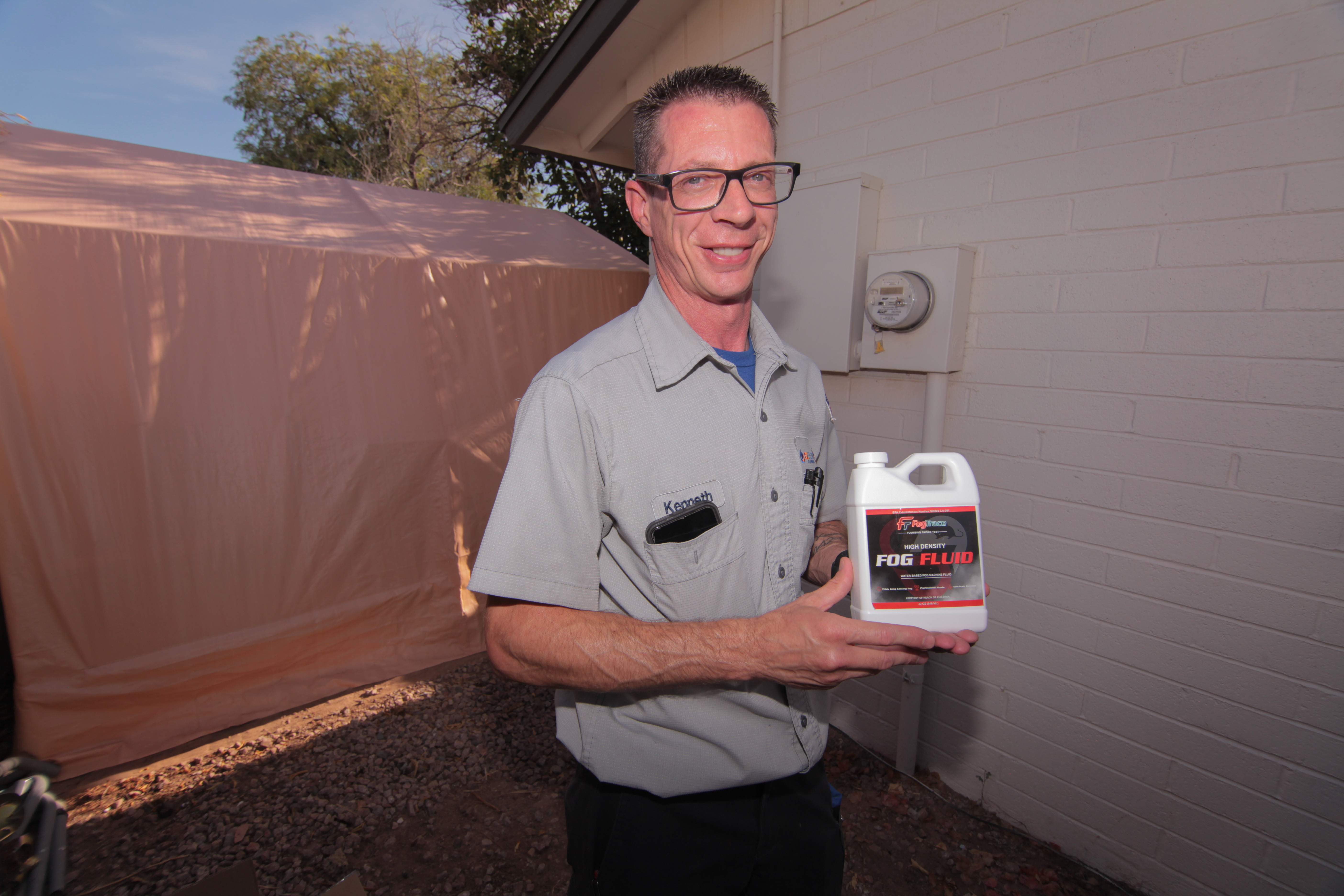 EZ Flow Plumbing technician holding a jug of FogTrace high-density fog fluid used for plumbing smoke testing in Gilbert, AZ